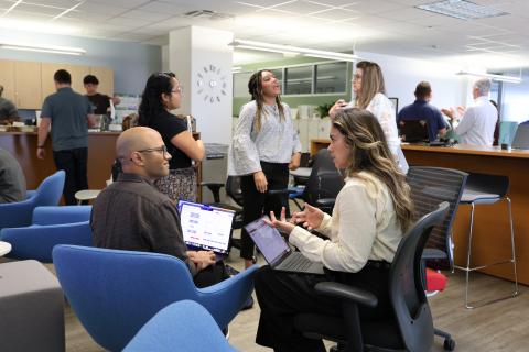 Two people with laptops talking to each other in a room with other people