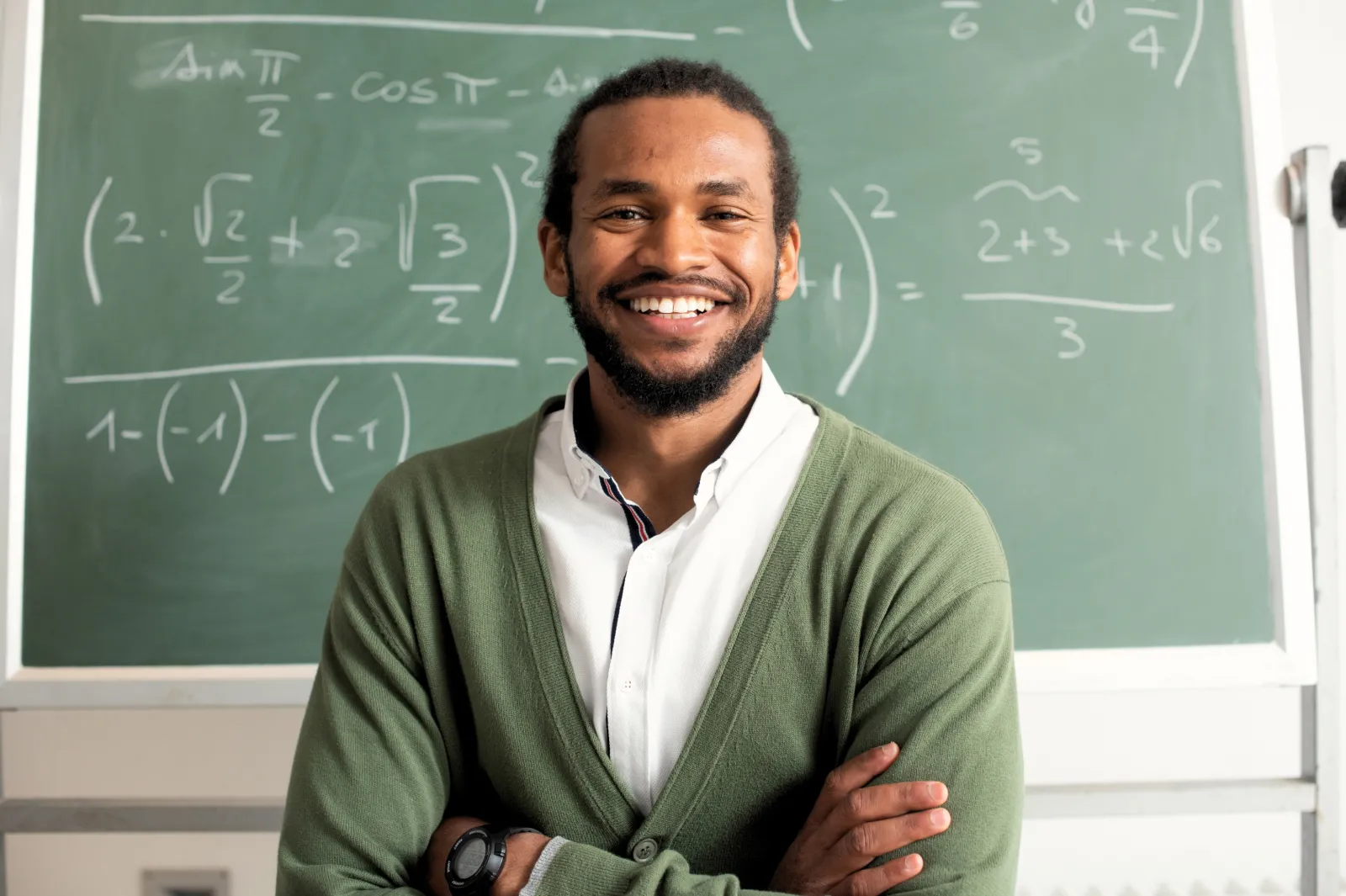 black male standing smiling in front of a chalk board