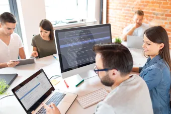 two people sitting around a desk working on computers