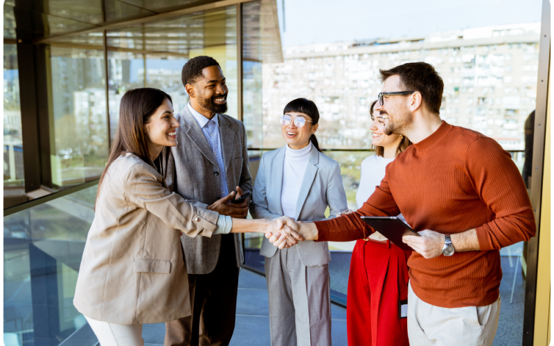 Image of 5 people having a conversation, two of the people are shaking hands.. 