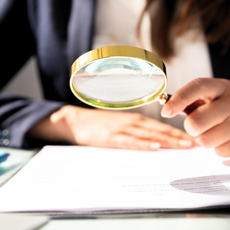 Person holding a magnifying glass looking a a piece of paper.